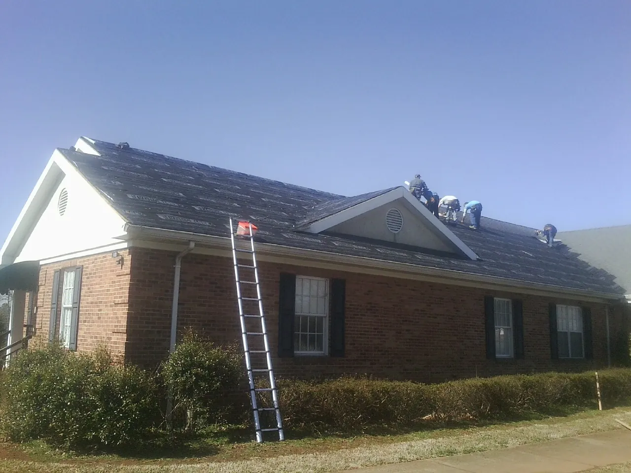 Crew tearing shingles off a brick ranch roof with a ladder set — Metal Roof Repair work by our crew in South Orange