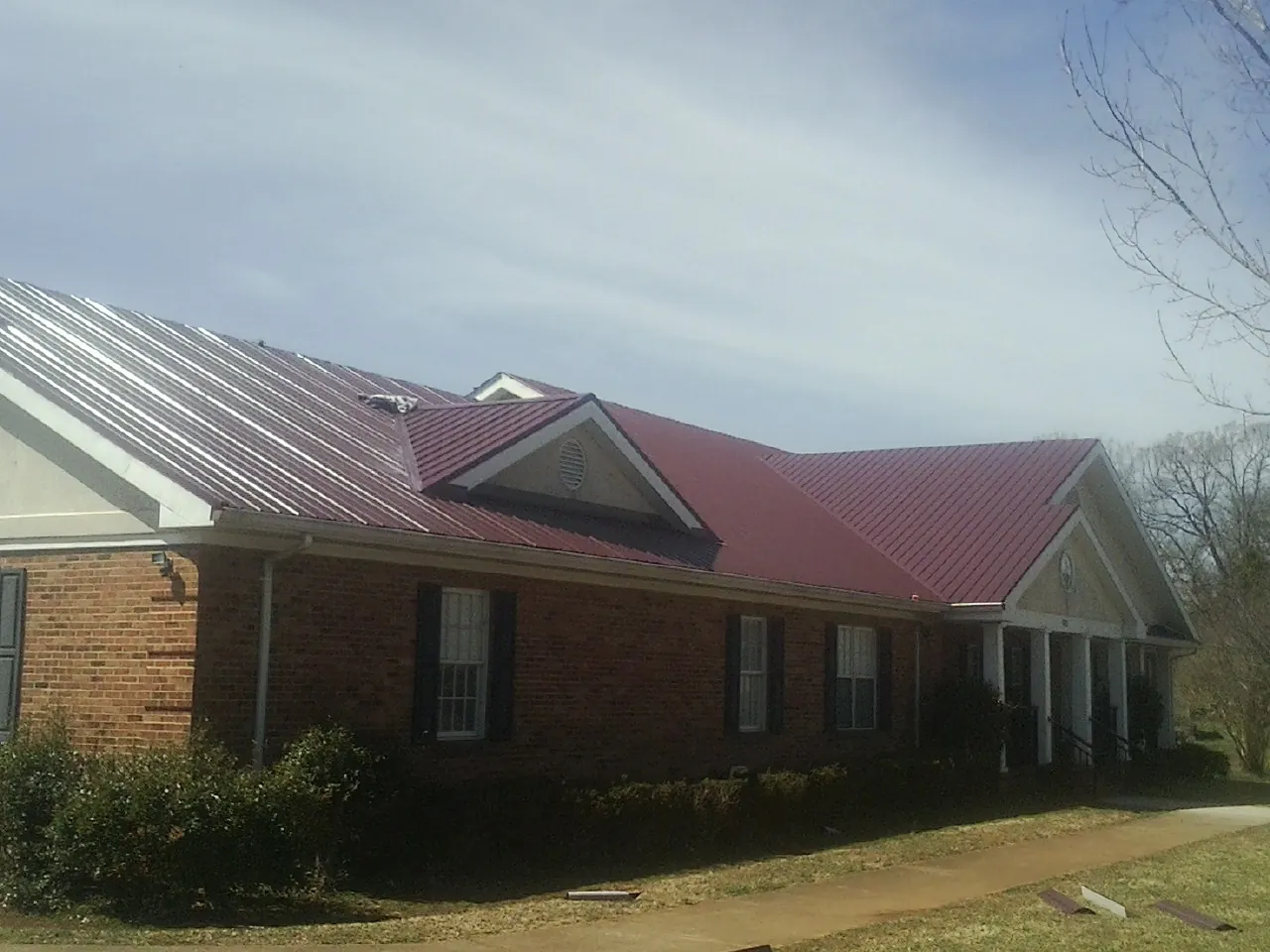 Red metal roof with gabled entries on a long brick building, from a Hail Damage Roof Repair job in South Orange