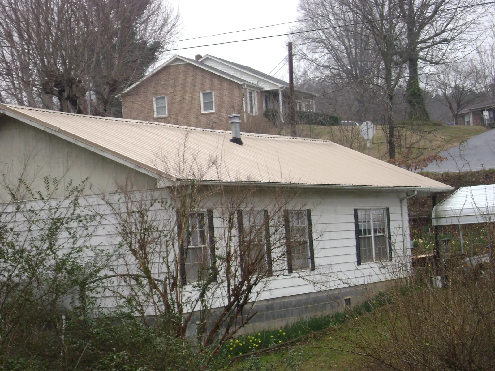 Tan metal roof on a white sided house set into a hillside — Commercial Roofing by Roofing Brothers in South Orange